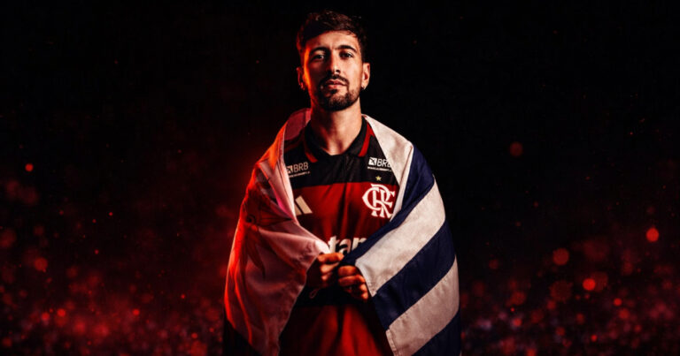 Arrascaeta posa com a camisa do Flamengo e a bandeira do Uruguai em imagem destacada sobre sua trajetória histórica no clube.